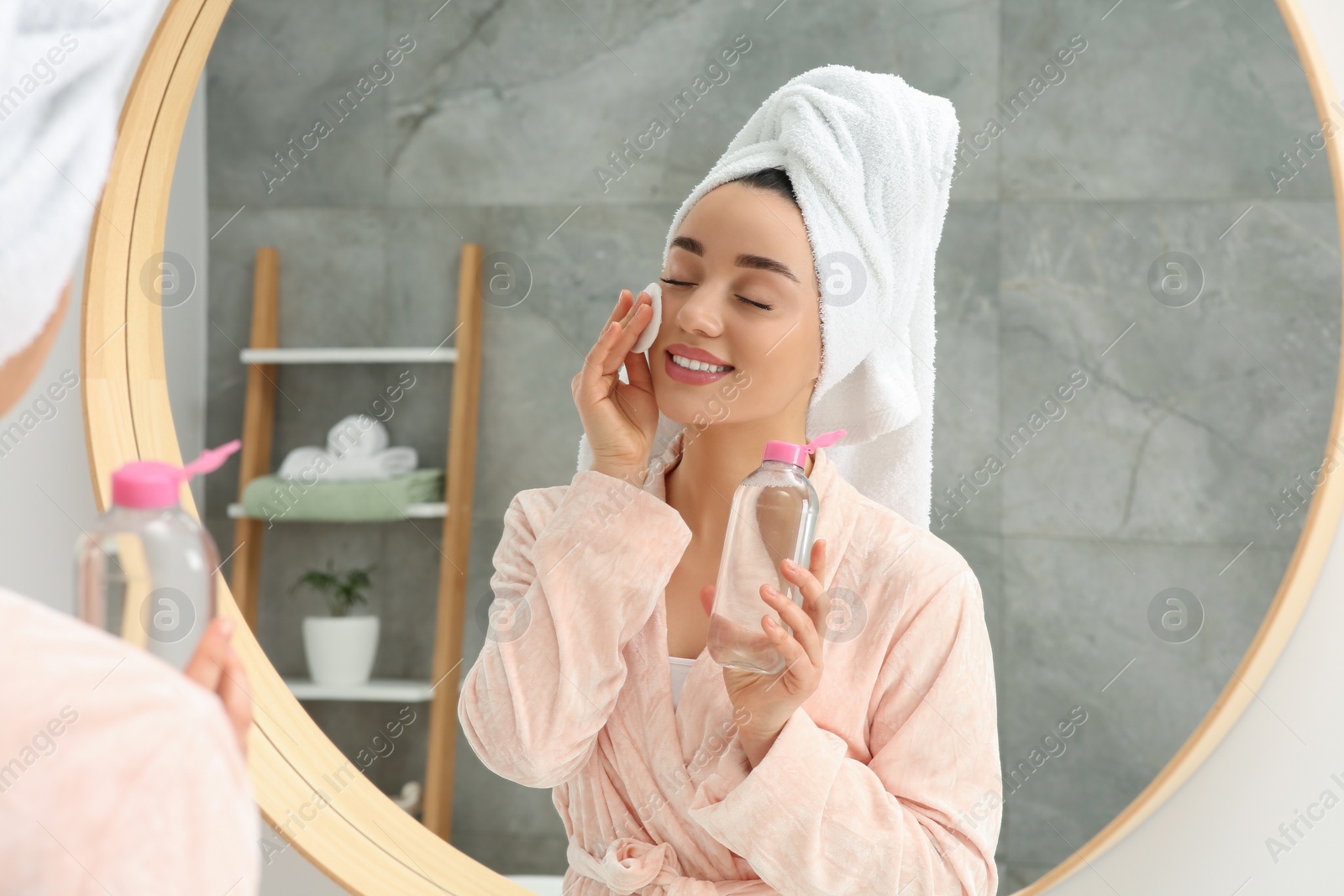 Photo of Beautiful woman in terry towel removing makeup with cotton pad near mirror indoors