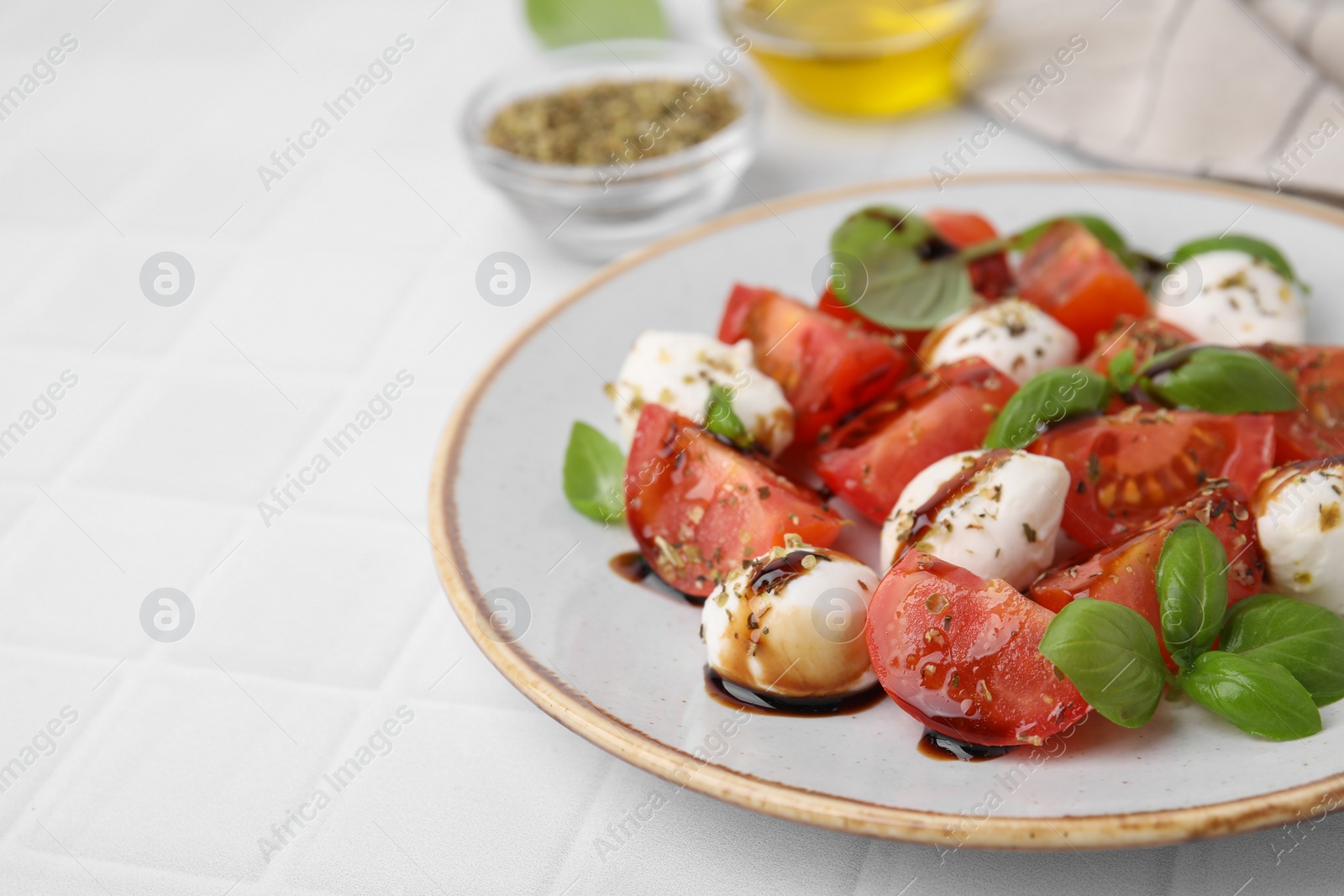 Photo of Tasty salad Caprese with mozarella balls, tomatoes, basil and sauce on white tiled table, closeup. Space for text