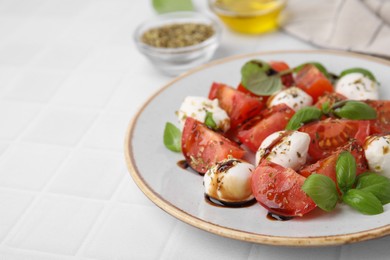 Photo of Tasty salad Caprese with mozarella balls, tomatoes, basil and sauce on white tiled table, closeup. Space for text