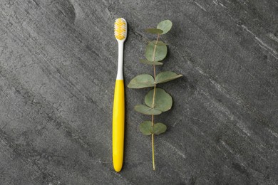 Photo of Plastic toothbrush and eucalyptus branch on grey table, flat lay