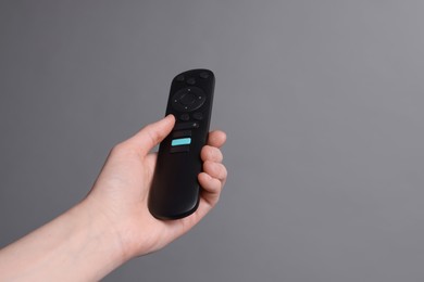 Woman holding TV remote control on grey background, closeup