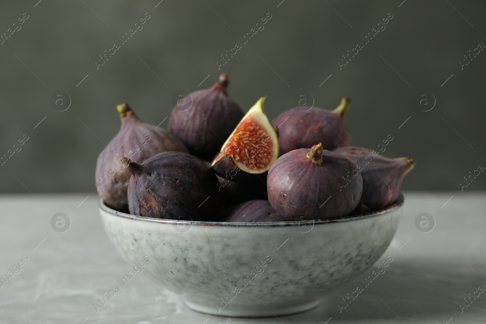 Photo of Tasty raw figs in bowl on light grey marble table, closeup