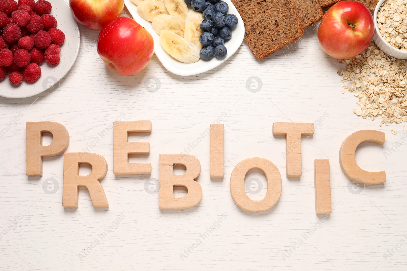 Photo of Flat lay composition with word Prebiotic made of wooden letters and different products on white table