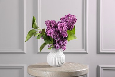 Photo of Beautiful lilac flowers in vase on wooden table near white wall