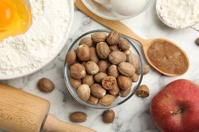 Photo of Nutmeg seeds and other ingredients for pastry on white marble table, flat lay