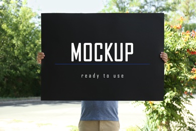 Man holding black poster with text Mockup Ready To Use outdoors