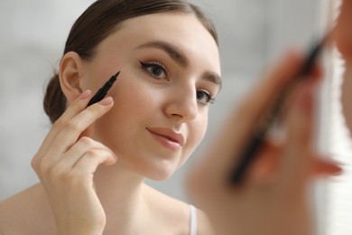 Photo of Makeup product. Woman applying black eyeliner indoors, closeup