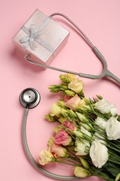 Photo of Stethoscope, gift box and flowers on pink background, flat lay. Happy Doctor's Day