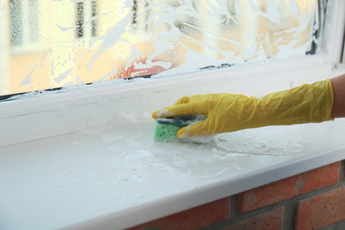 Photo of Woman cleaning window sill with sponge, closeup