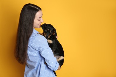 Young woman with cute puppy on yellow background. Space for text