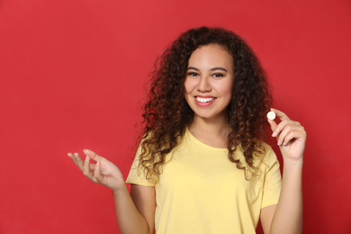 Photo of African-American woman with vitamin pill on red background