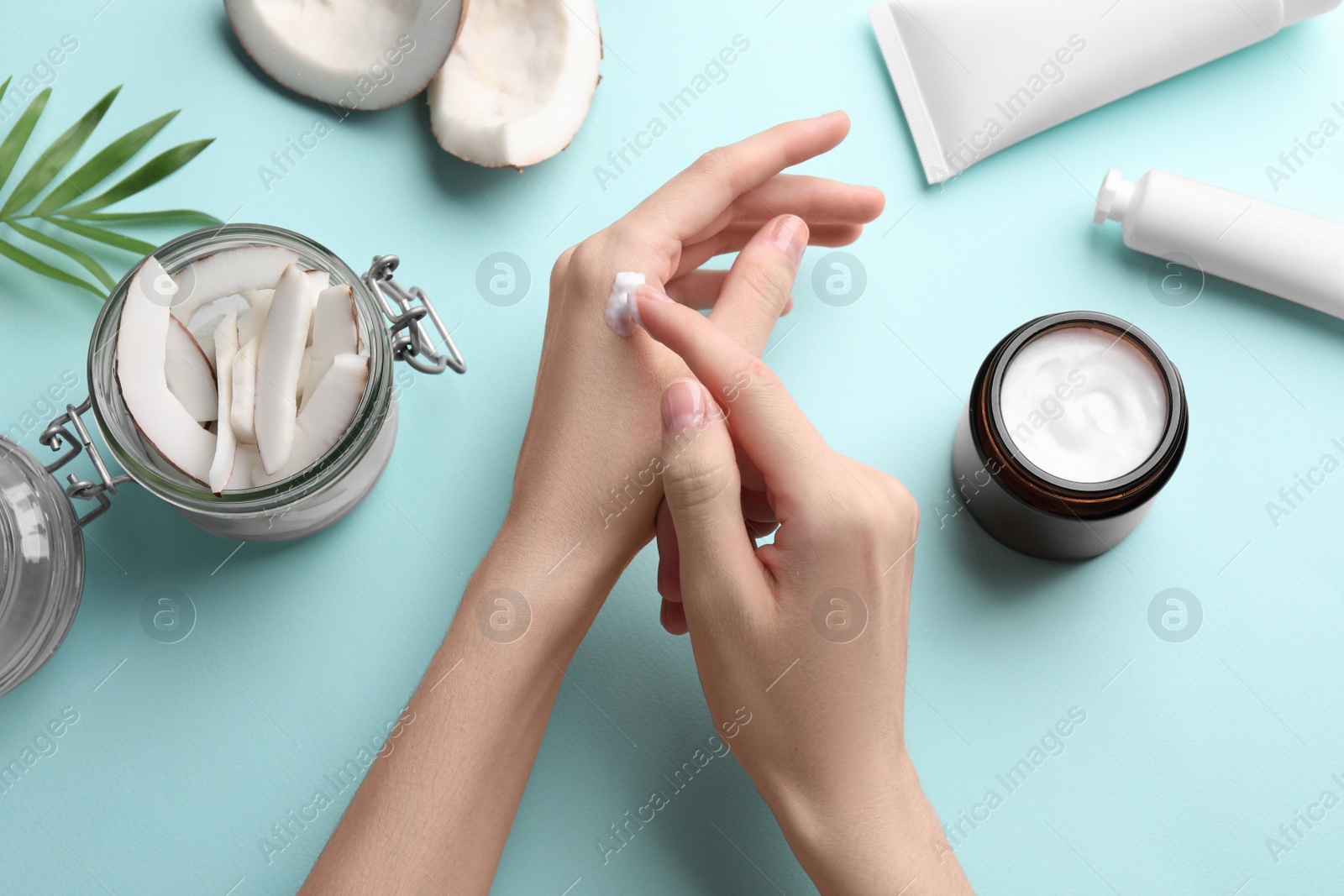 Photo of Woman applying hand cream on turquoise background, top view