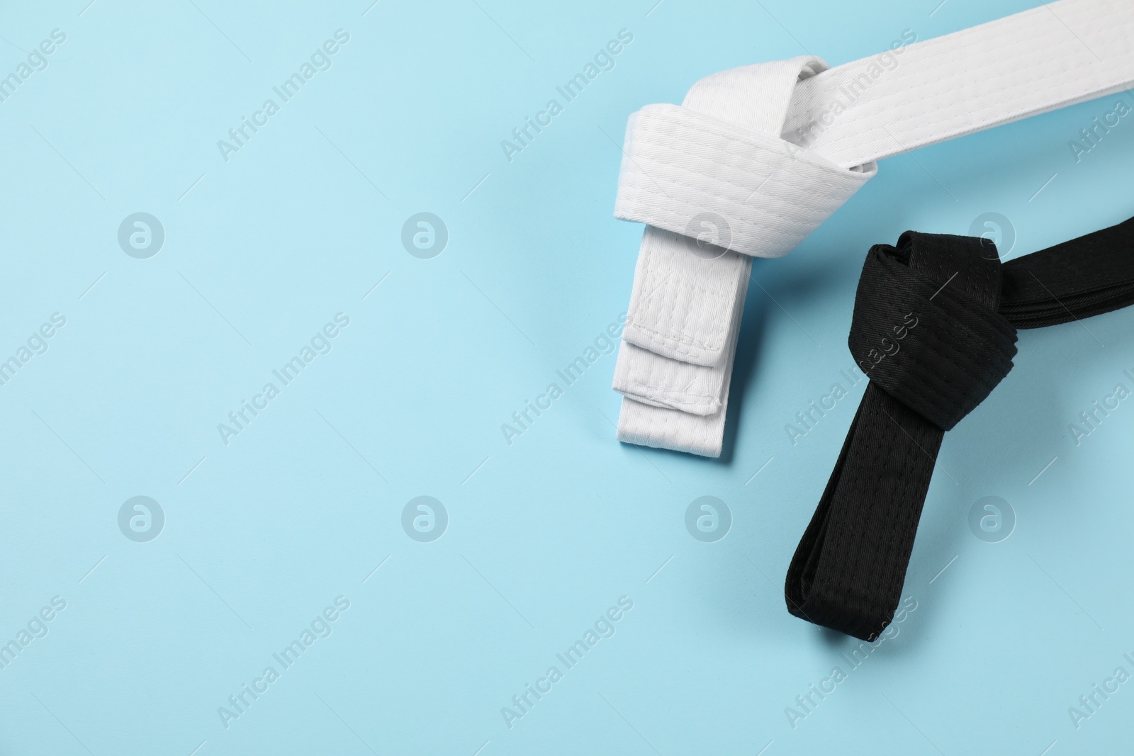 Photo of White and black karate belts on light blue background, flat lay. Space for text