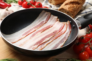 Slices of raw bacon in frying pan and fresh products on table, closeup