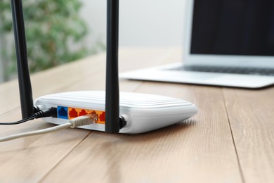 Modern Wi-Fi router and laptop on wooden table indoors, closeup