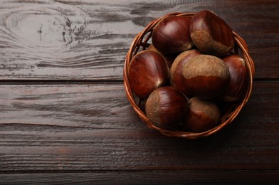 Sweet fresh edible chestnuts in wicker bowl on wooden table, top view. Space for text