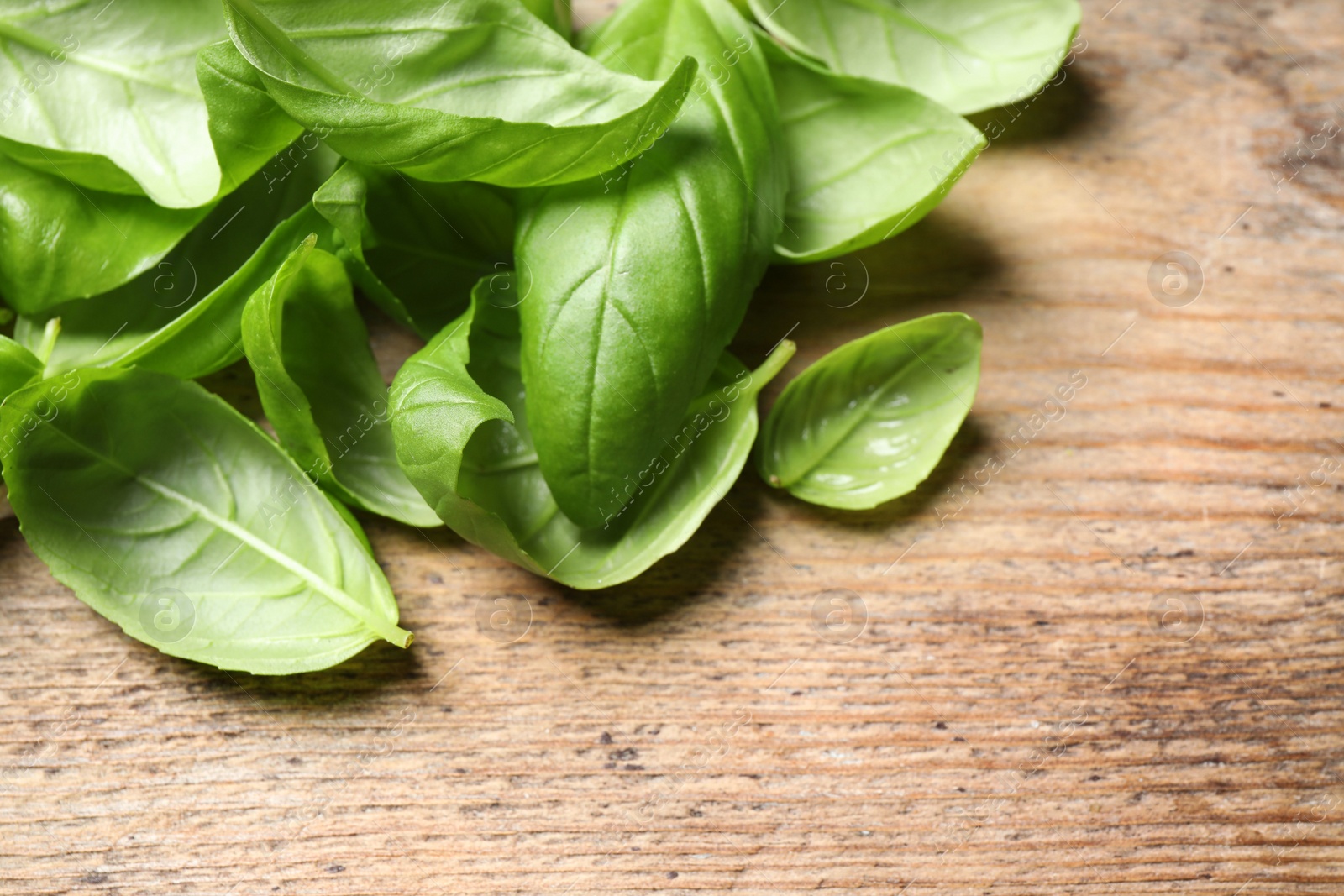 Photo of Fresh basil leaves on wooden table, closeup