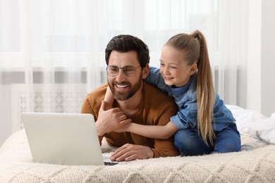 Photo of Happy man and his daughter with laptop on bed at home