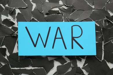 Photo of Word War and pieces of torn black paper on white background, flat lay
