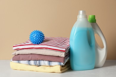 Photo of Blue dryer ball and stacked clean clothes near laundry detergents on white table