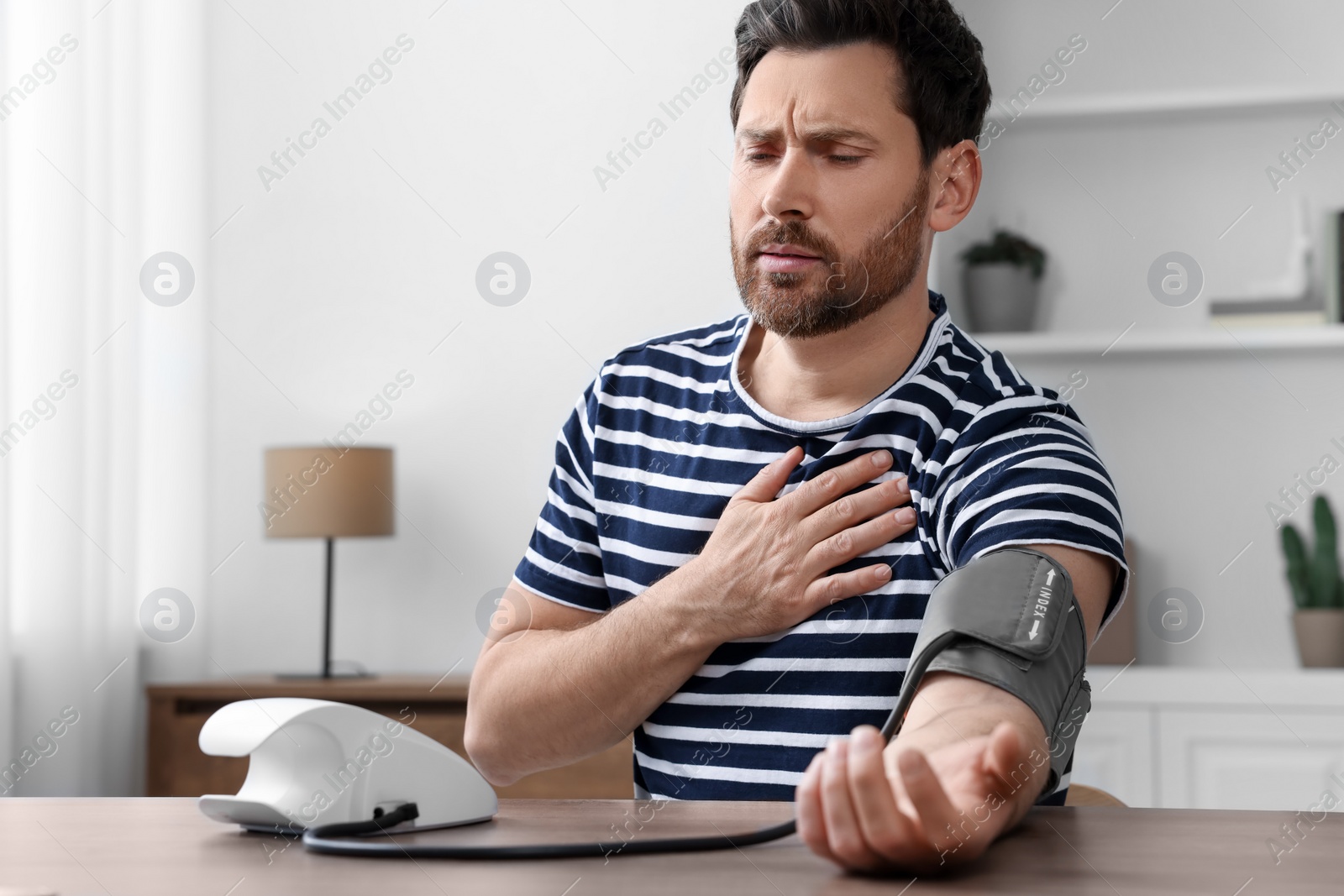 Photo of Man suffering from heartache and measuring blood pressure in room, space for text