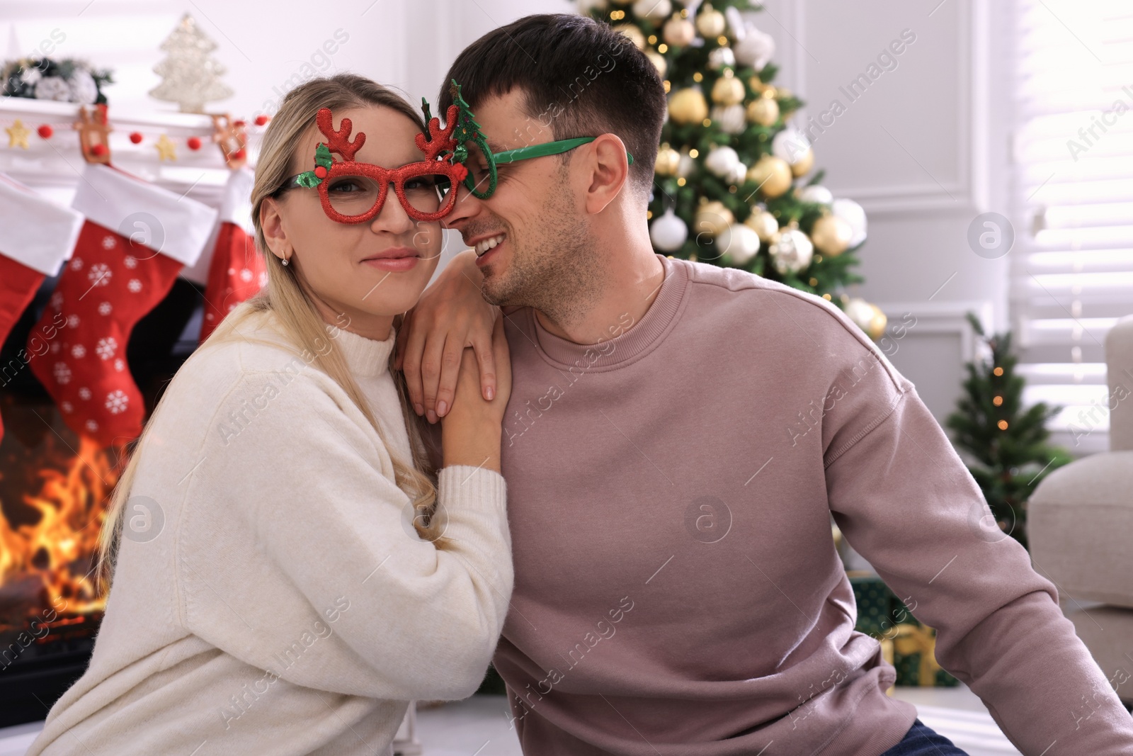 Photo of Lovely couple wearing party glasses in room decorated for Christmas