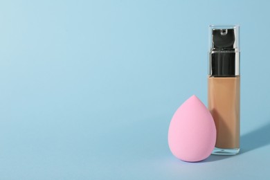 Photo of Pink makeup sponge and skin foundation on light blue background. Space for text
