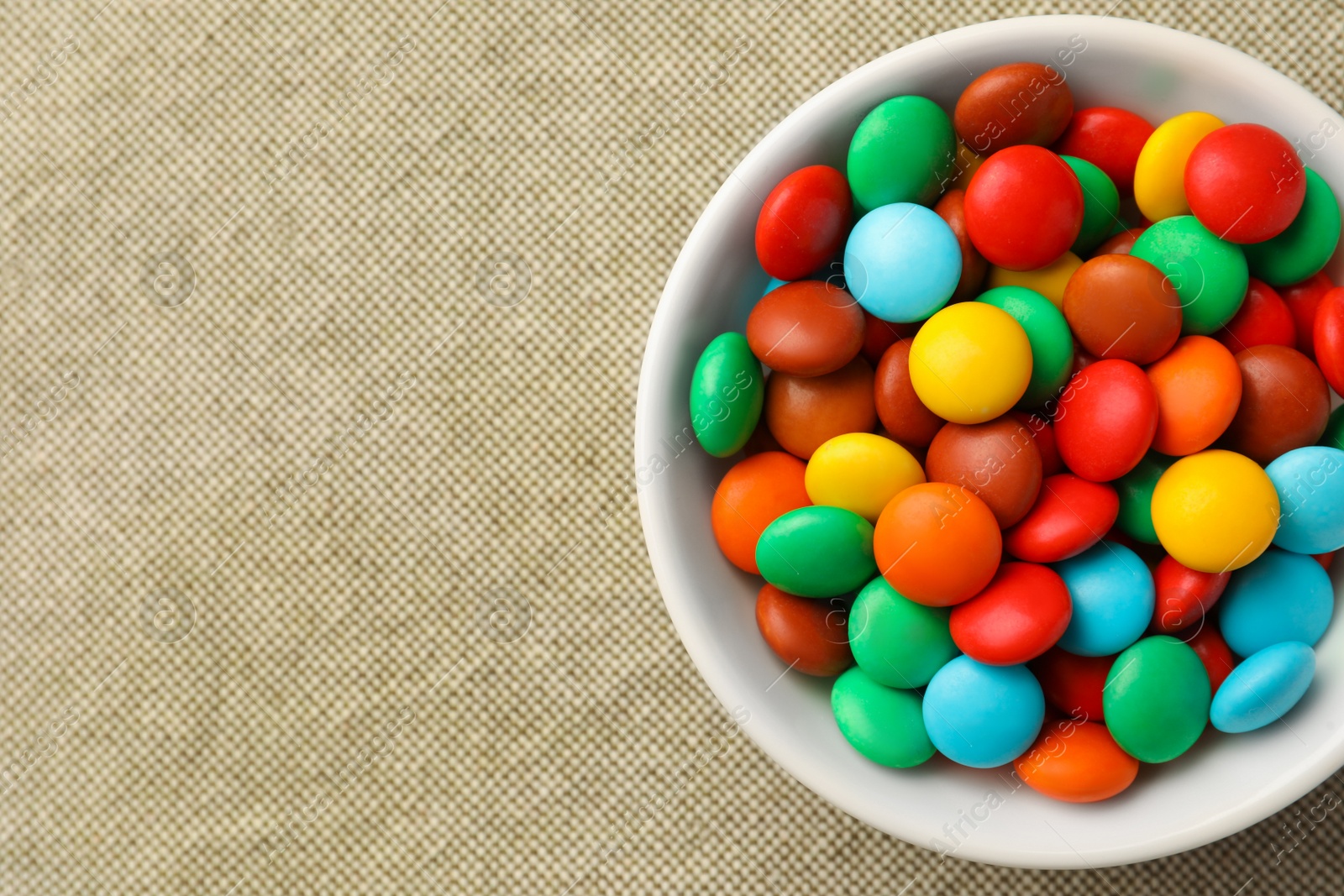 Photo of Bowl with tasty colorful candies on cloth, top view. Space for text