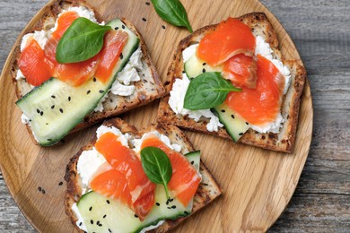 Delicious sandwiches with cream cheese, salmon, cucumber and spinach on wooden table, top view