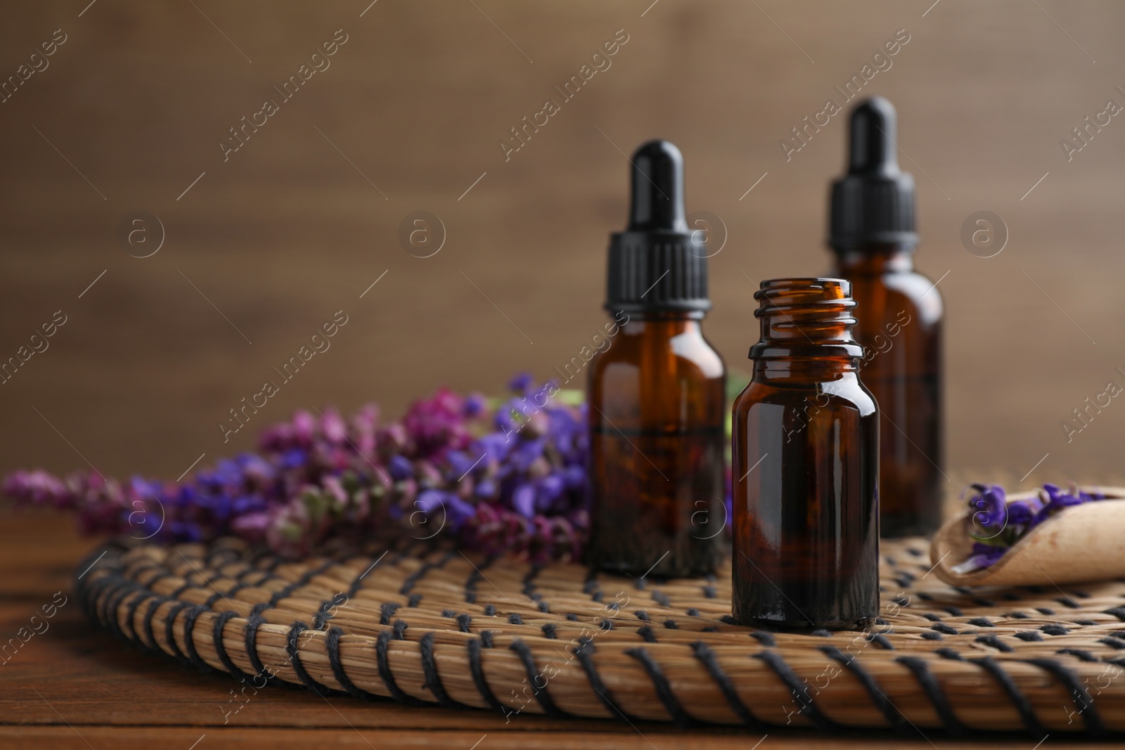 Photo of Bottles of sage essential oil and flowers on table, space for text