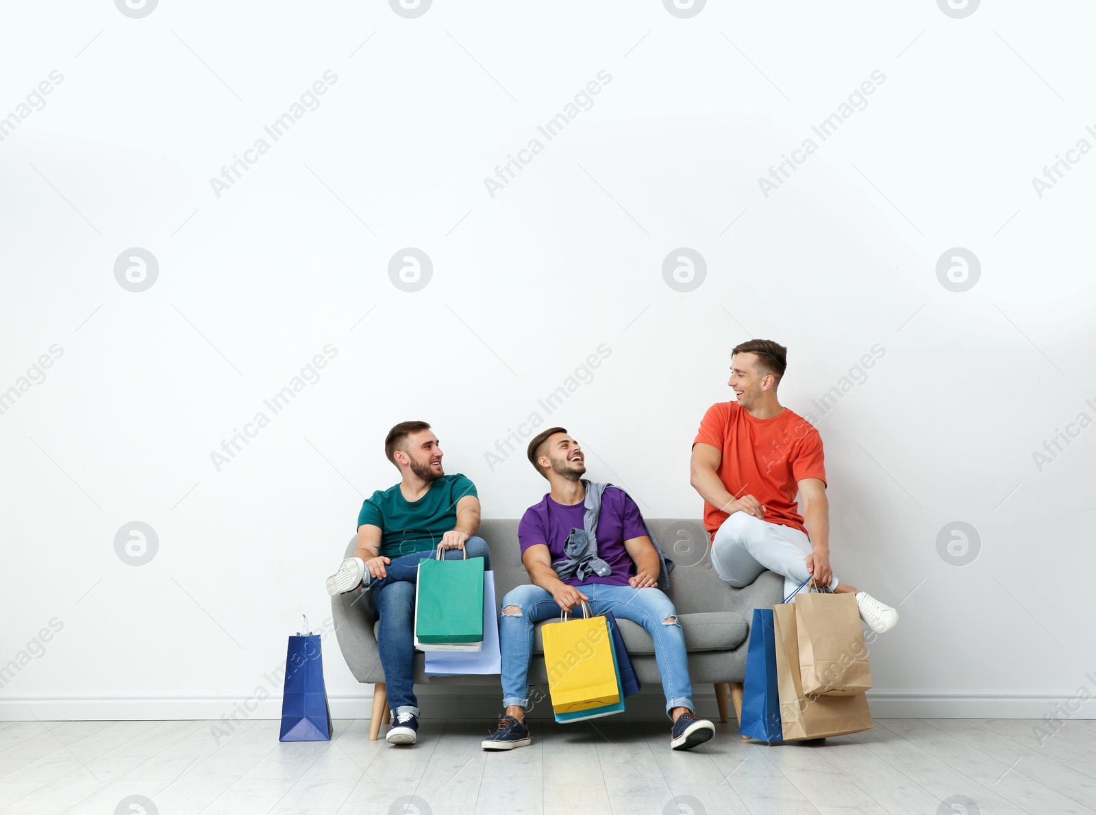 Photo of Group of young men with shopping bags sitting on sofa near light wall