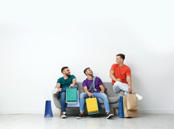 Group of young men with shopping bags sitting on sofa near light wall