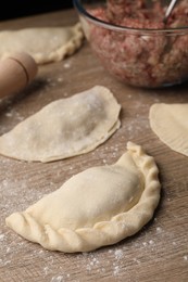Photo of Uncooked chebureki, minced meat and rolling pin on wooden table
