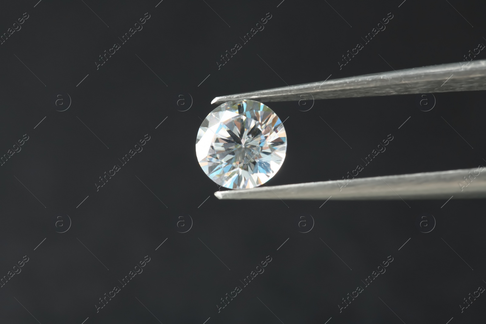 Photo of Tweezers with beautiful shiny diamond on gray background, closeup. Space for text