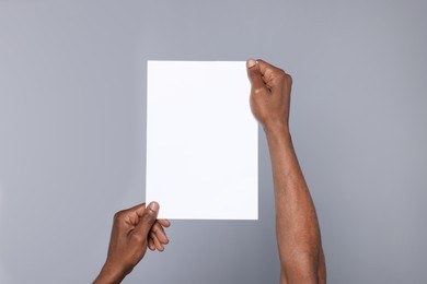 Photo of African American man holding sheet of paper on grey background, closeup. Mockup for design