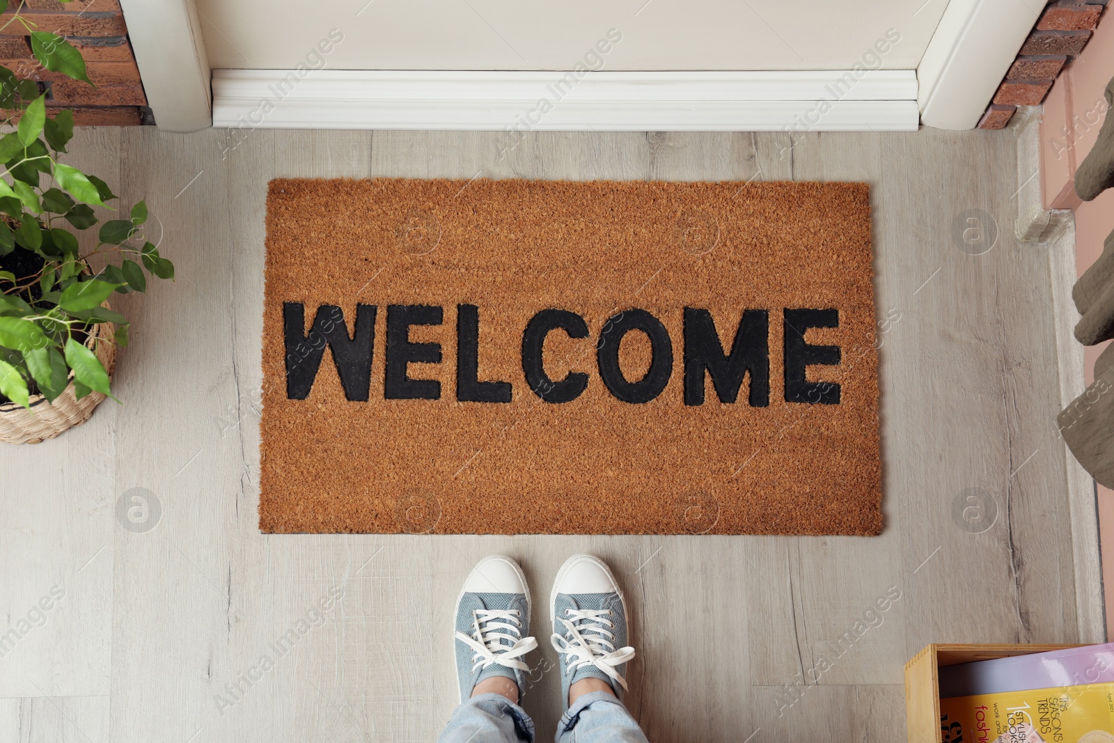 Photo of Woman standing near door mat with word Welcome on wooden floor in hall, top view