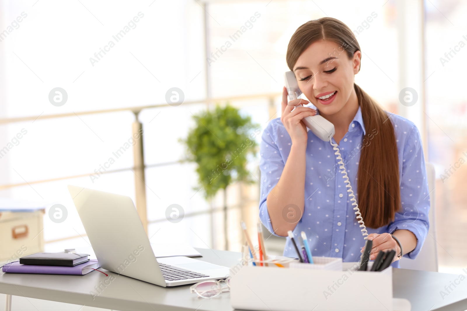 Photo of Young woman talking on phone at workplace