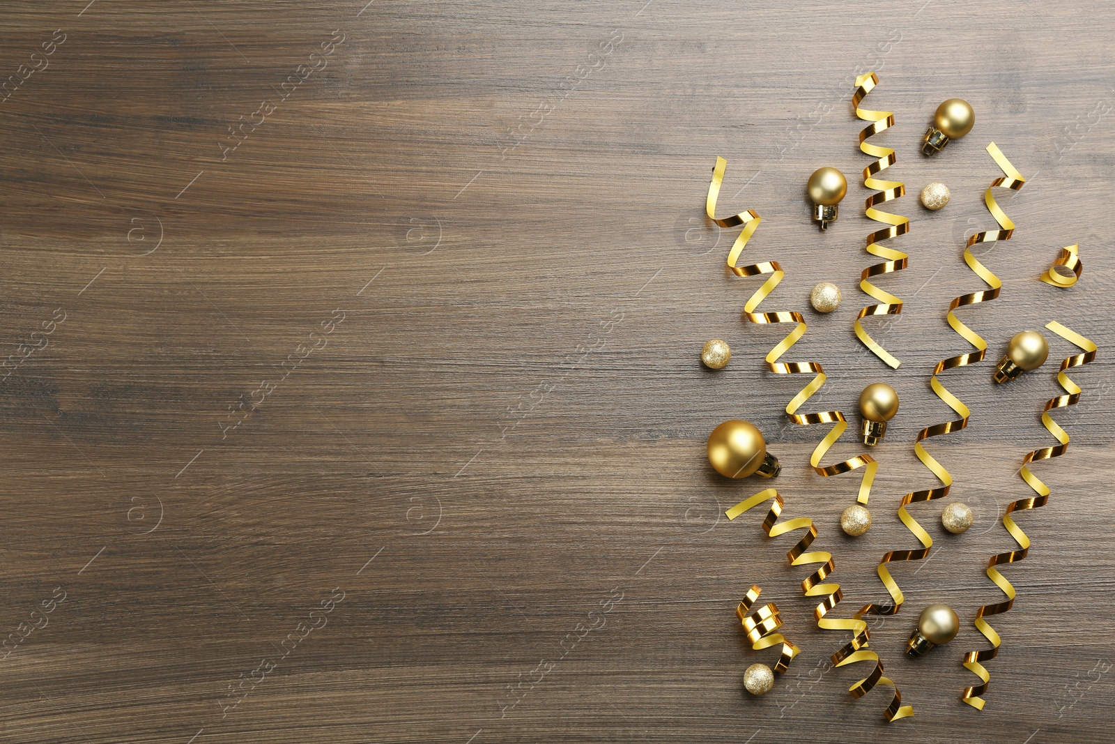 Photo of Shiny serpentine streamers and Christmas balls on wooden background, flat lay. Space for text