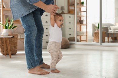 Photo of Father supporting his baby daughter while she learning to walk at home