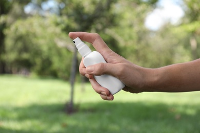 Woman with bottle of insect repellent spray outdoors, closeup