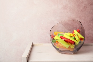 Colorful paper pieces for lottery in glass vase on wooden table. Space for text