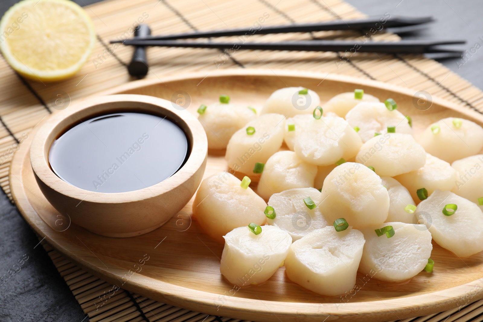 Photo of Raw scallops with green onion and soy sauce on dark table, closeup