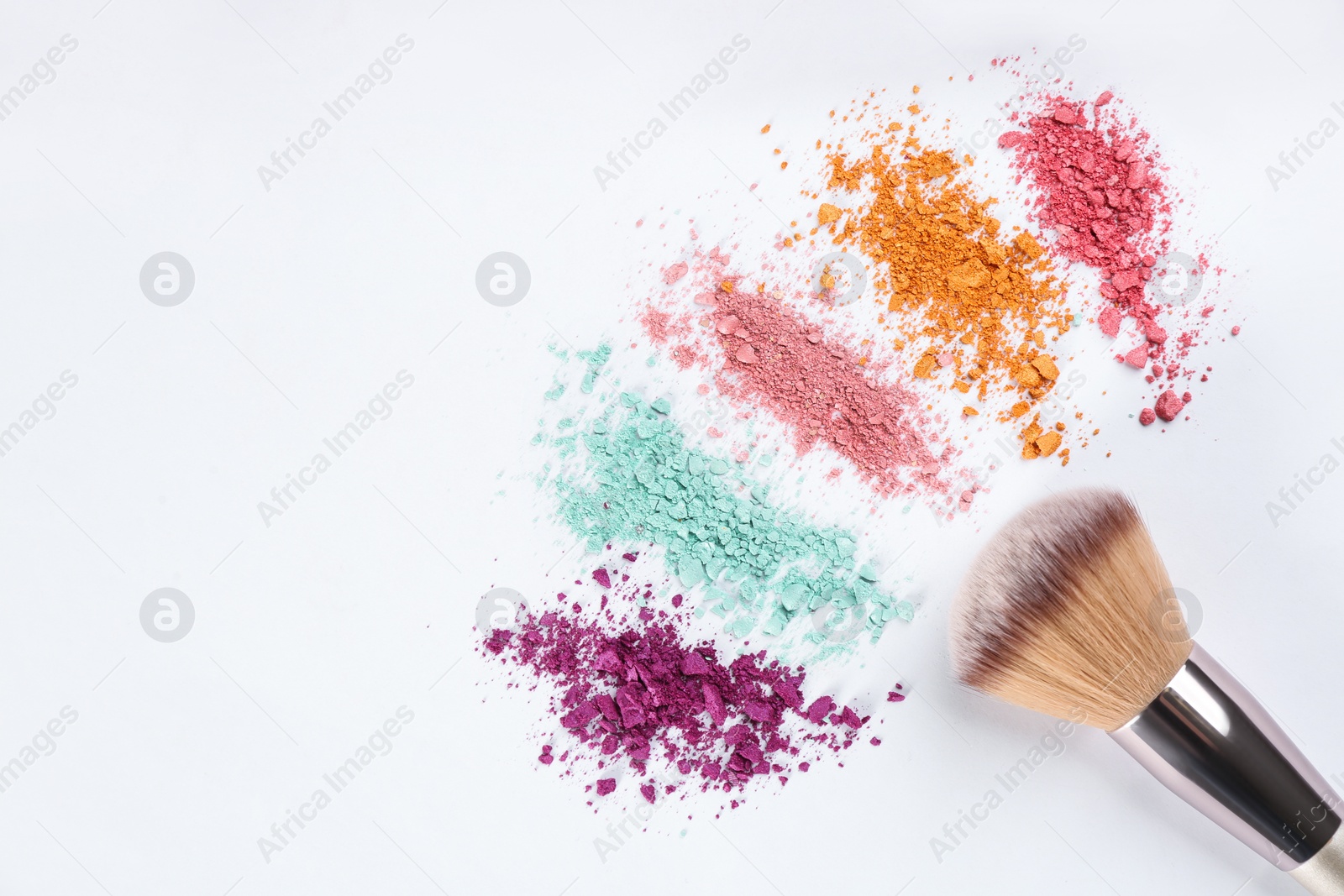 Photo of Makeup brush and scattered eye shadows on white background, flat lay. Space for text