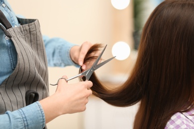 Barber making stylish haircut with professional scissors in beauty salon, closeup