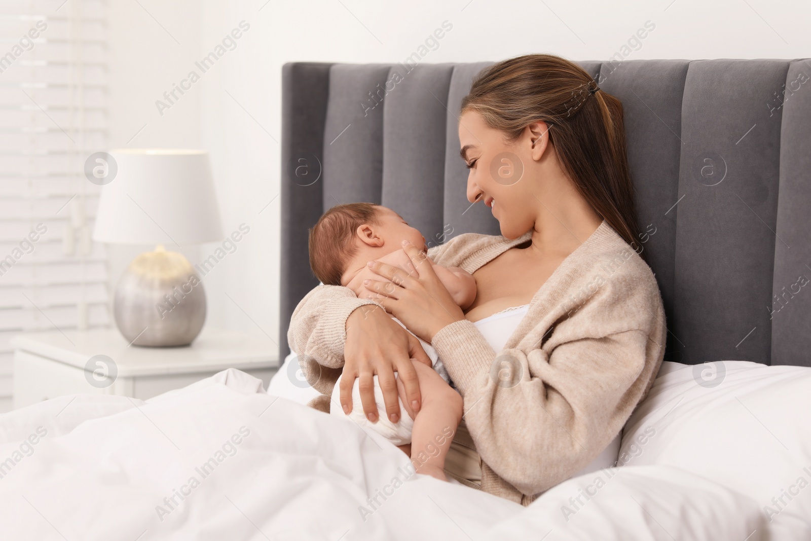 Photo of Mother holding her cute newborn baby in bed indoors, space for text