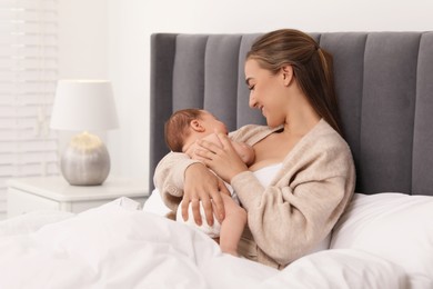 Mother holding her cute newborn baby in bed indoors, space for text