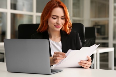 Woman with papers working near laptop at white desk in office