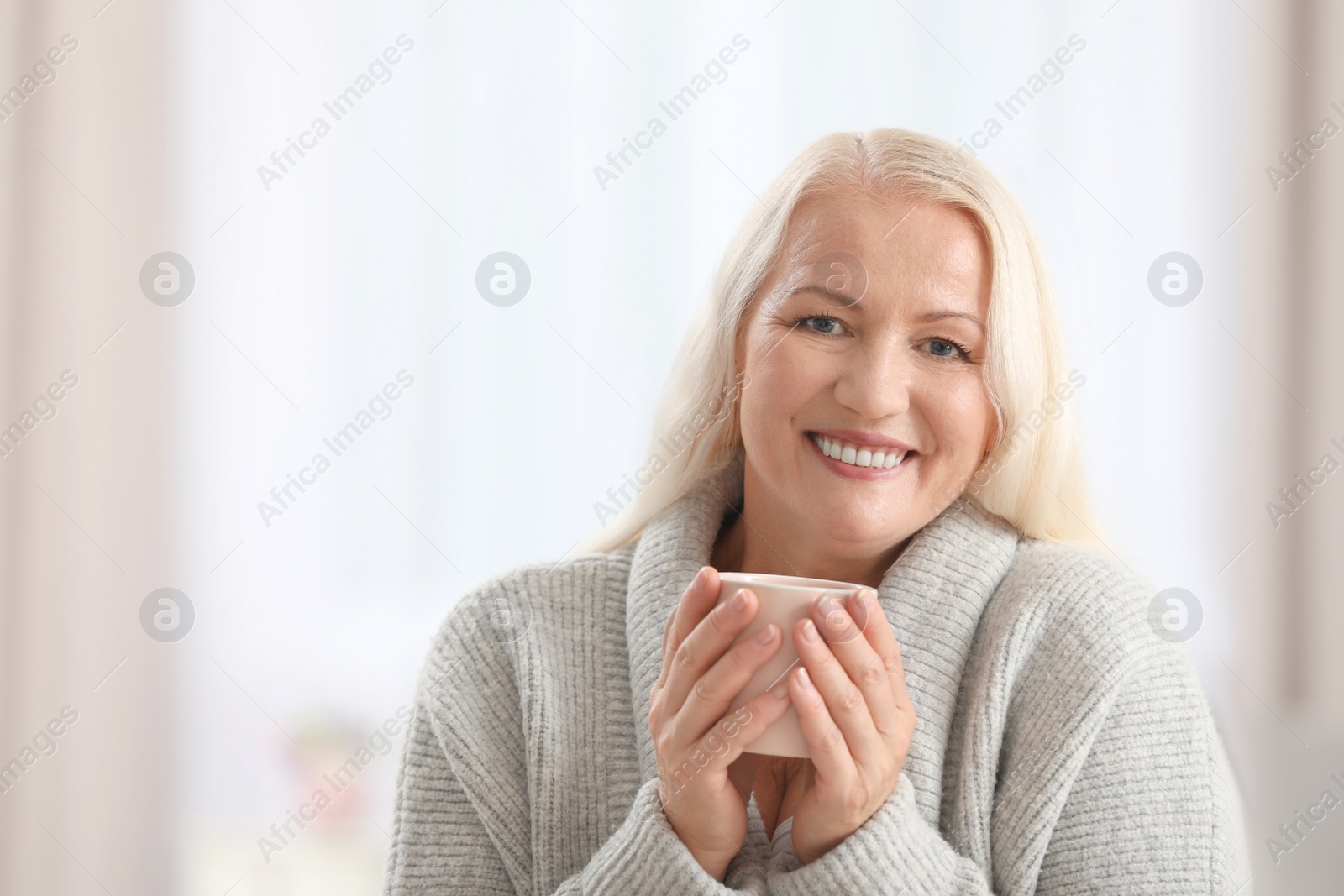 Photo of Portrait of beautiful older woman with cup of tea against blurred background