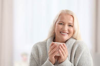 Portrait of beautiful older woman with cup of tea against blurred background
