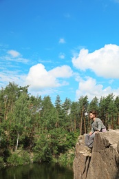 Young man on rock near lake and forest. Camping season